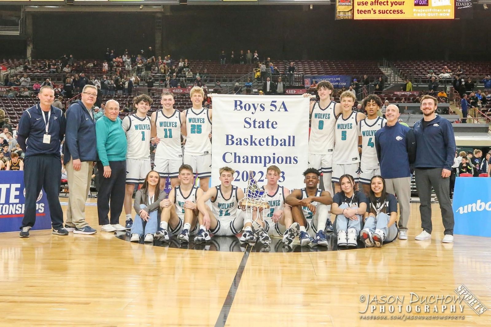 Lake City boys basketball team and coaches with the 2023 Boys 5A State Champions banner